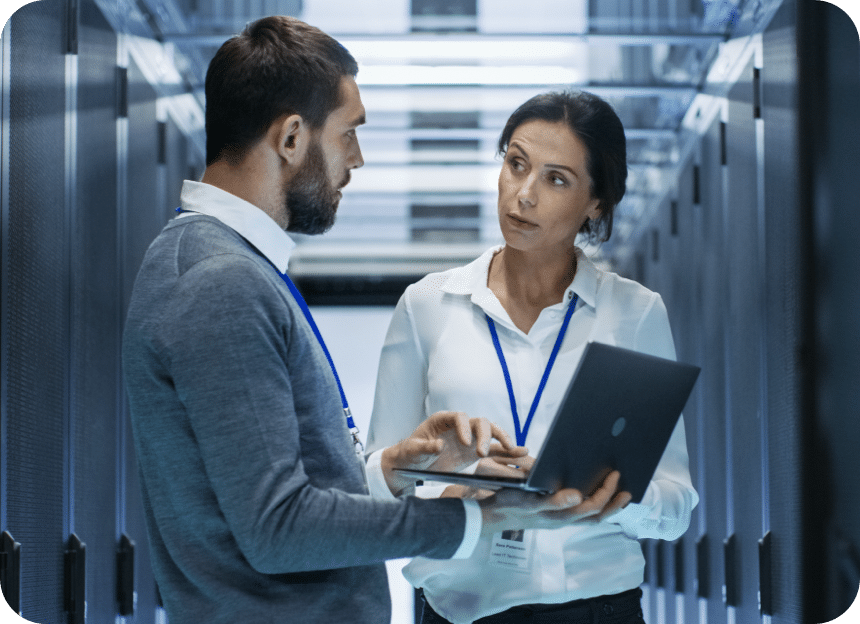 un homme et une femme debout dans une salle de serveurs regardant un ordinateur portable